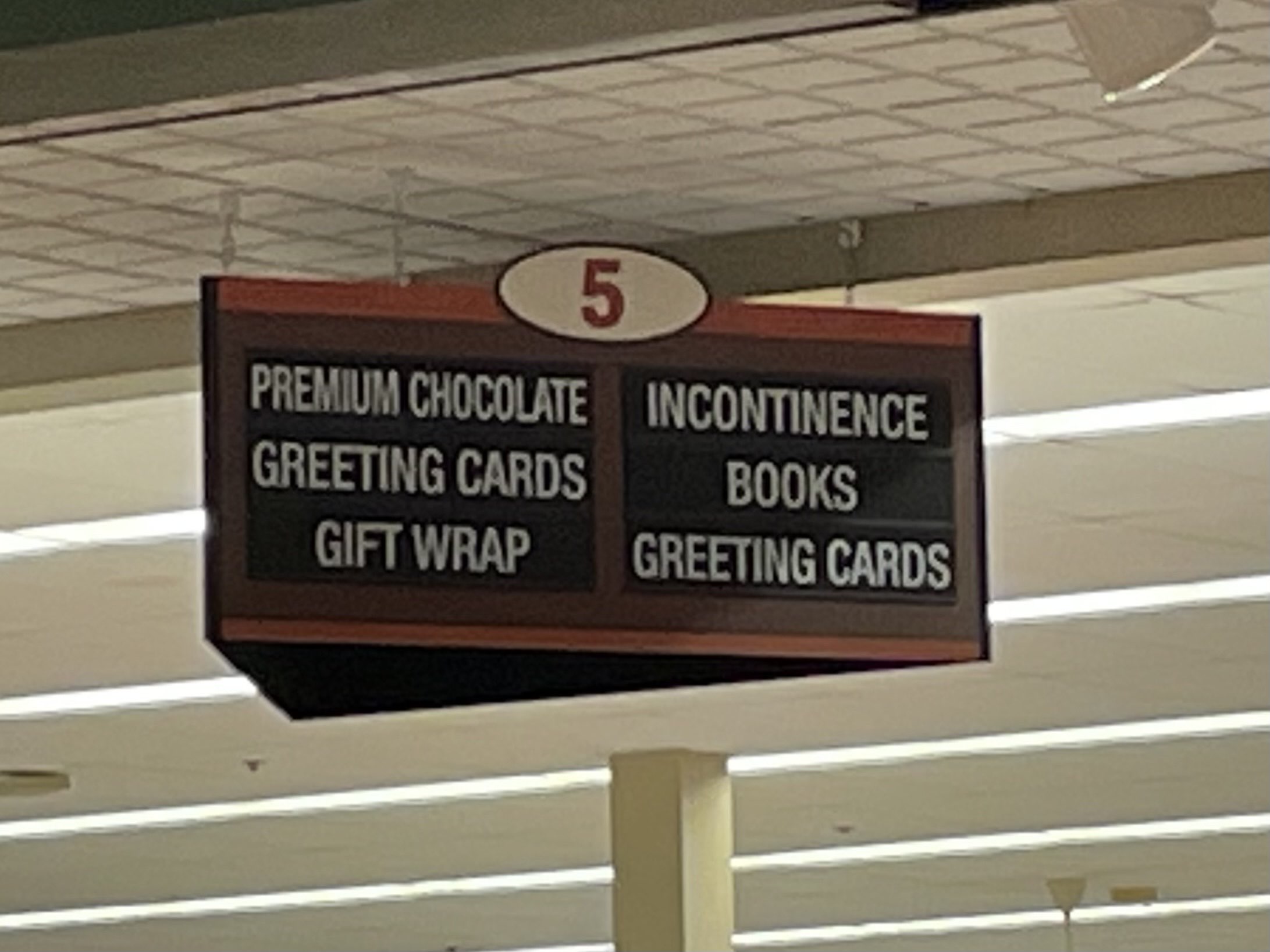 A grocery store aisle sign advertising, among other things, Premium Choclate and Incontinence.